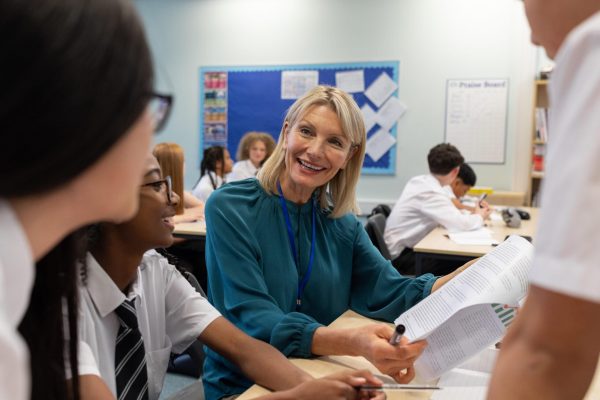 Close-up shot of a small group of students and their teacher sitting in a classroom in a school in Newcastle upon Tyne, North East England. The main focus is on the smiling teacher who is showing the students a worksheet. The students are wearing school uniforms.

Videos similar to this scenario available.